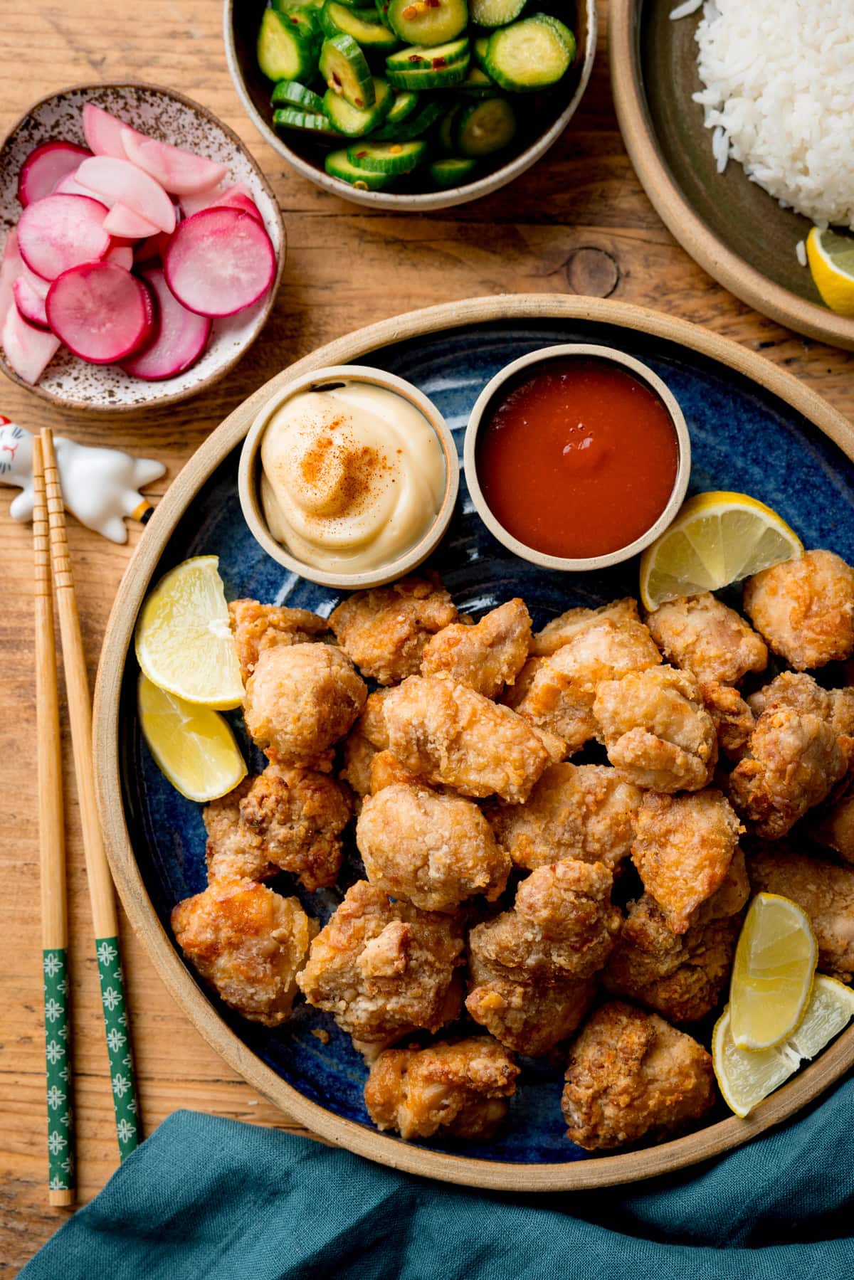 A plate of Air Fryer Chicken Karaage with lemon wedges, served with mayonnaise, sriracha, pickled radishes, cucumber salad, and a side of white rice.