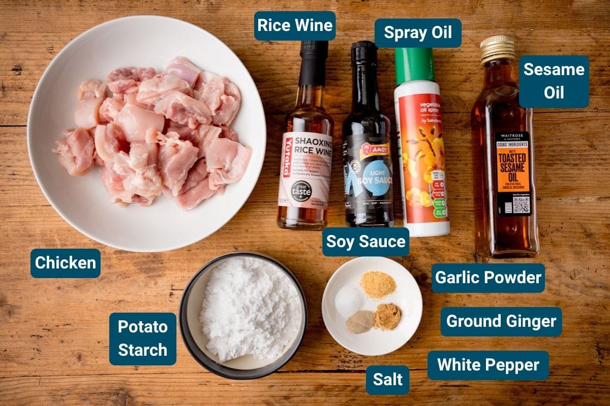 A bowl of raw chicken, potato starch, seasonings, and sauces sits on a wooden surface.