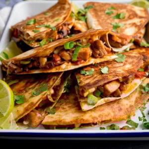 A plate of grilled Chicken Quesadilla filled with diced chicken, vegetables, and melted cheese, garnished with chopped coriander and lime wedges.