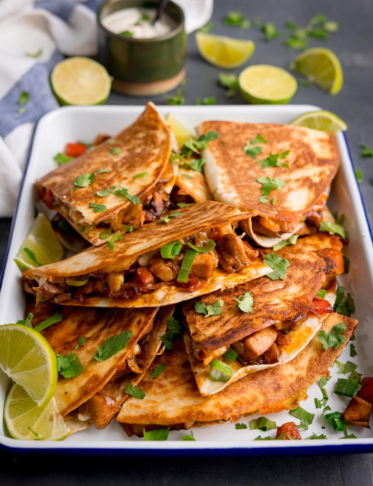 Una bandeja de quesadillas de pollo llenas de verduras y adornada con cilantro picado, servido con rodajas de lima.