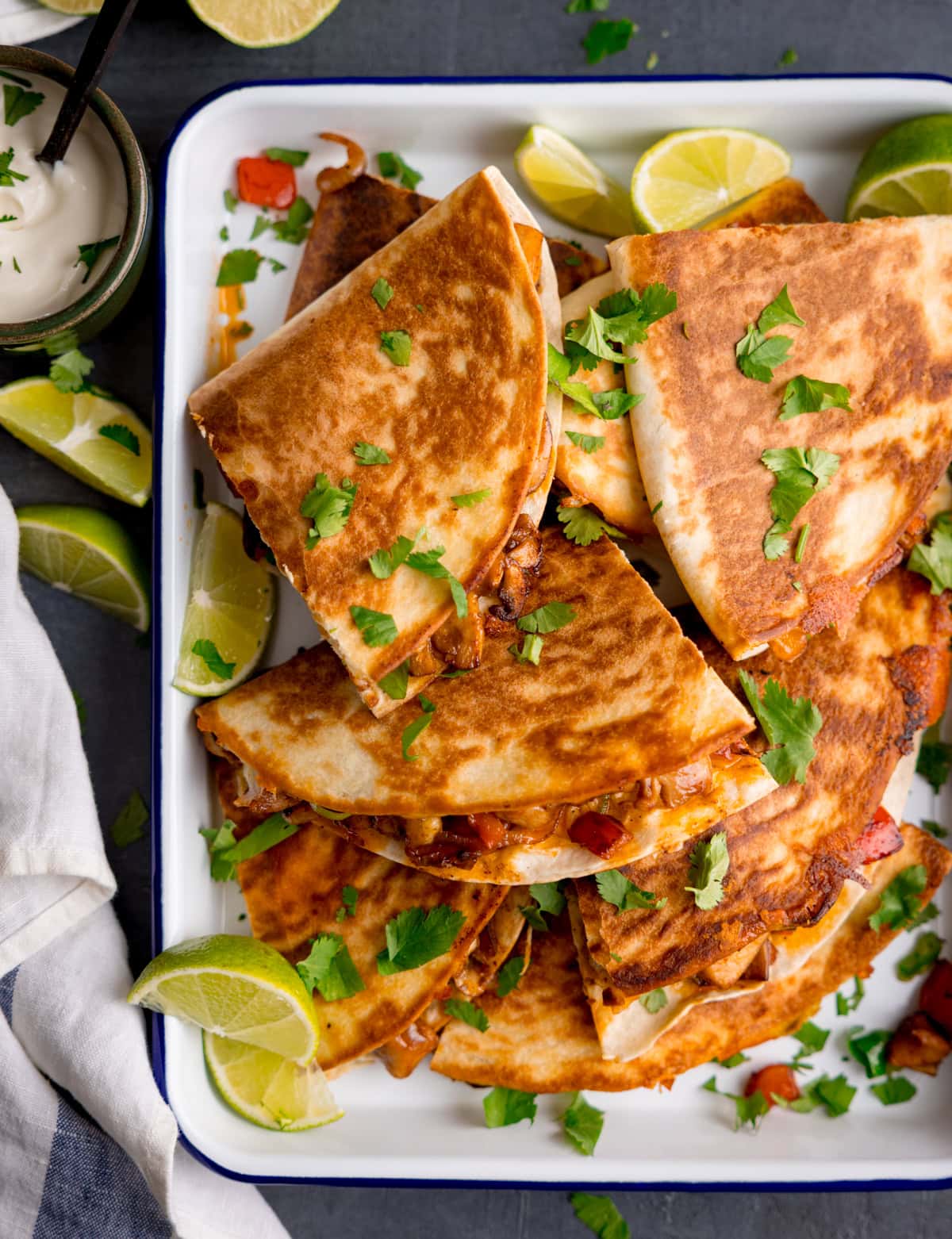 Un plato de quesadillas de pollo adornada con cilantro fresco y rodajas de lima, servidas con un lado de salsa cremosa.