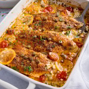 Baked fish in lemon sauce with cherry tomatoes, capers, and herbs in a creamy dressing.