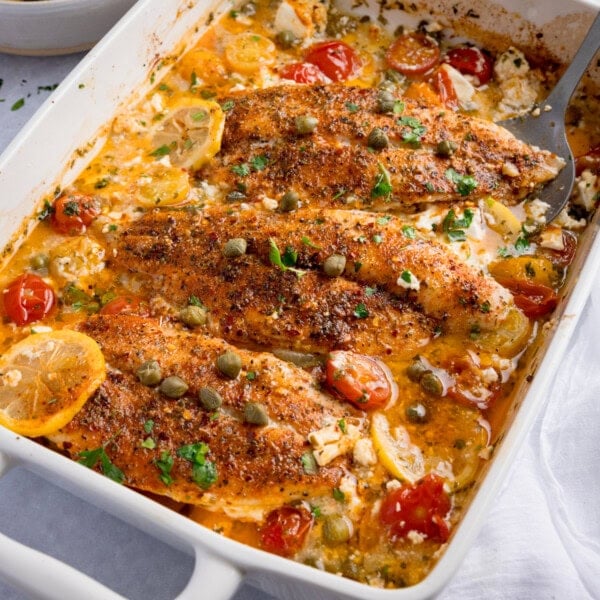 Baked fish in lemon sauce with cherry tomatoes, capers, and herbs in a creamy dressing.