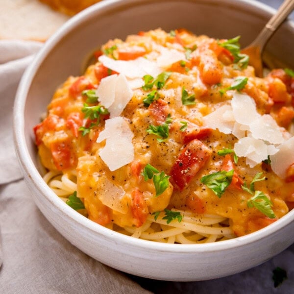A bowl of spaghetti topped with a creamy lentil and red pepper sauce, garnished with fresh parsley, black pepper, and shaved parmesan cheese.