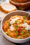 A bowl of spaghetti topped with creamy red lentil sauce, garnished with shaved parmesan and parsley, with slices of bread in the background.