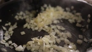 Diced onions being sautéed in a black frying pan.