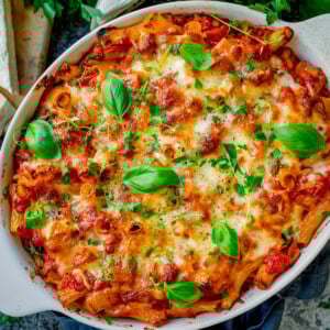 Sausage Pasta Bake topped with melted cheese and fresh basil leaves in a white oval dish.