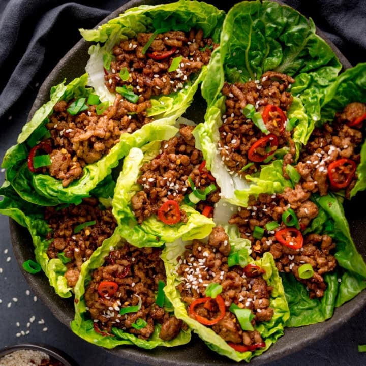 A plate of turkey lettuce wraps filled with savoury minced meat, garnished with sliced red chilli, spring onions, and sesame seeds.