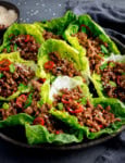 A plate of turkey mince lettuce wraps filled with seasoned meat, topped with sliced red chillies, chopped spring onions, and sesame seeds.