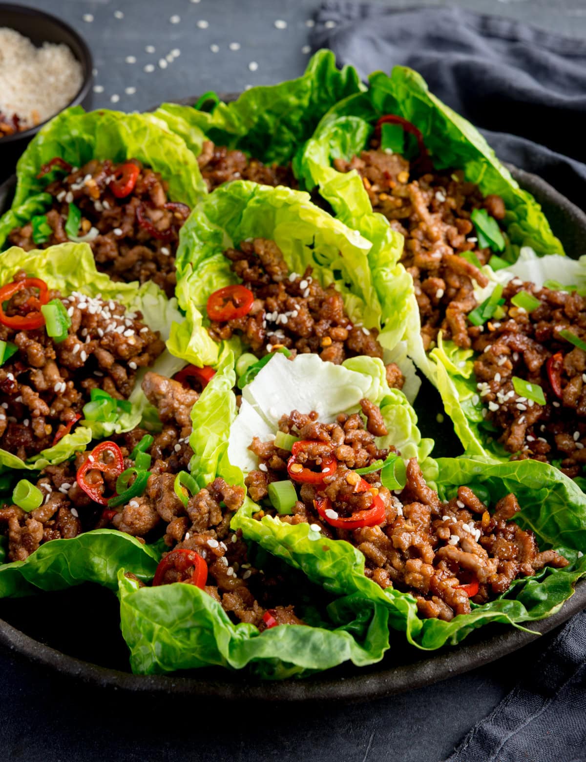 A plate of turkey mince lettuce wraps filled with seasoned meat, topped with sliced red chillies, chopped spring onions, and sesame seeds.