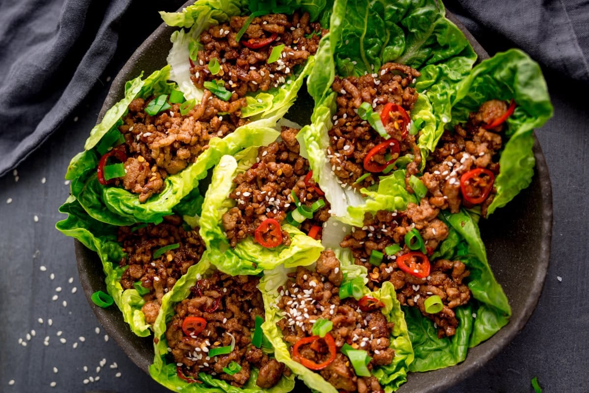 A plate of Turkey Lettuce Wraps filled with cooked minced turkey, sliced red chilli, chopped spring onions, and sprinkled with sesame seeds.