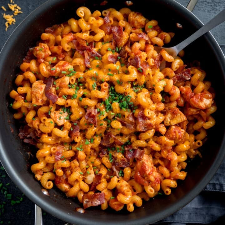 A frying pan cooked pasta in creamy tomato sauce, topped with BBQ chicken, crispy bacon, and chopped chives.