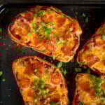 Slices of bread topped with melted cheese, pepperoni, halved cherry tomatoes, and chopped spring onions.