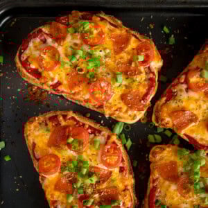 Slices of bread topped with melted cheese, pepperoni, halved cherry tomatoes, and chopped spring onions.