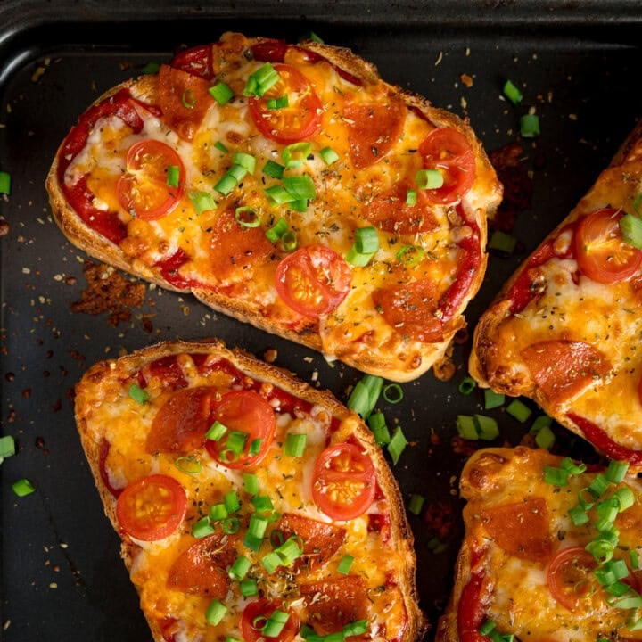 Slices of bread topped with melted cheese, pepperoni, halved cherry tomatoes, and chopped spring onions.