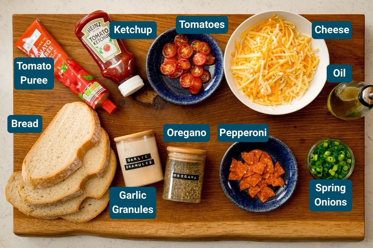 Una tabla de madera con ingredientes etiquetados para tostadas de pizza: pan, puré de tomate, tomate ketchup, tomates, queso, aceite, cebolletas, pepperoni, orégano y gránulos de ajo.