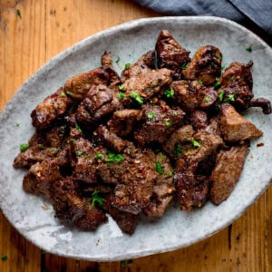 A plate of cooked, seasoned air fryer steak pieces garnished with chopped herbs, served on a ceramic dish atop a wooden table.