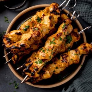 Air Fryer chicken tikka kebabs with cilantro served on a round plate atop a dark surface.