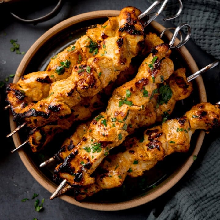 Air Fryer chicken tikka kebabs with cilantro served on a round plate atop a dark surface.