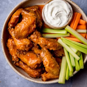 Square overhead image of a plate of buffalo air fryer wings, served with celery, carrot batons and blue cheese dip.
