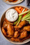 Tall overhead image of a plate of buffalo air fryer wings, served with celery, carrot batons and blue cheese dip.