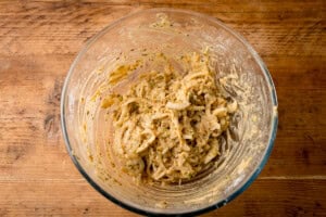 A glass bowl filled with sliced onions coated in a seasoned gram-flour-based-batter for an Onion Bhaji recipe. The bowl is on a wooden surface.