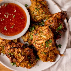 Overhead square image of a plate of crispy air fryer onion bhajis served with a bowl of sweet chilli sauce.