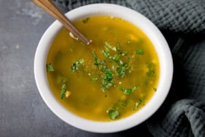 Melted cilantro garlic butter in a small white bowl with a gold teaspoon sticking out.