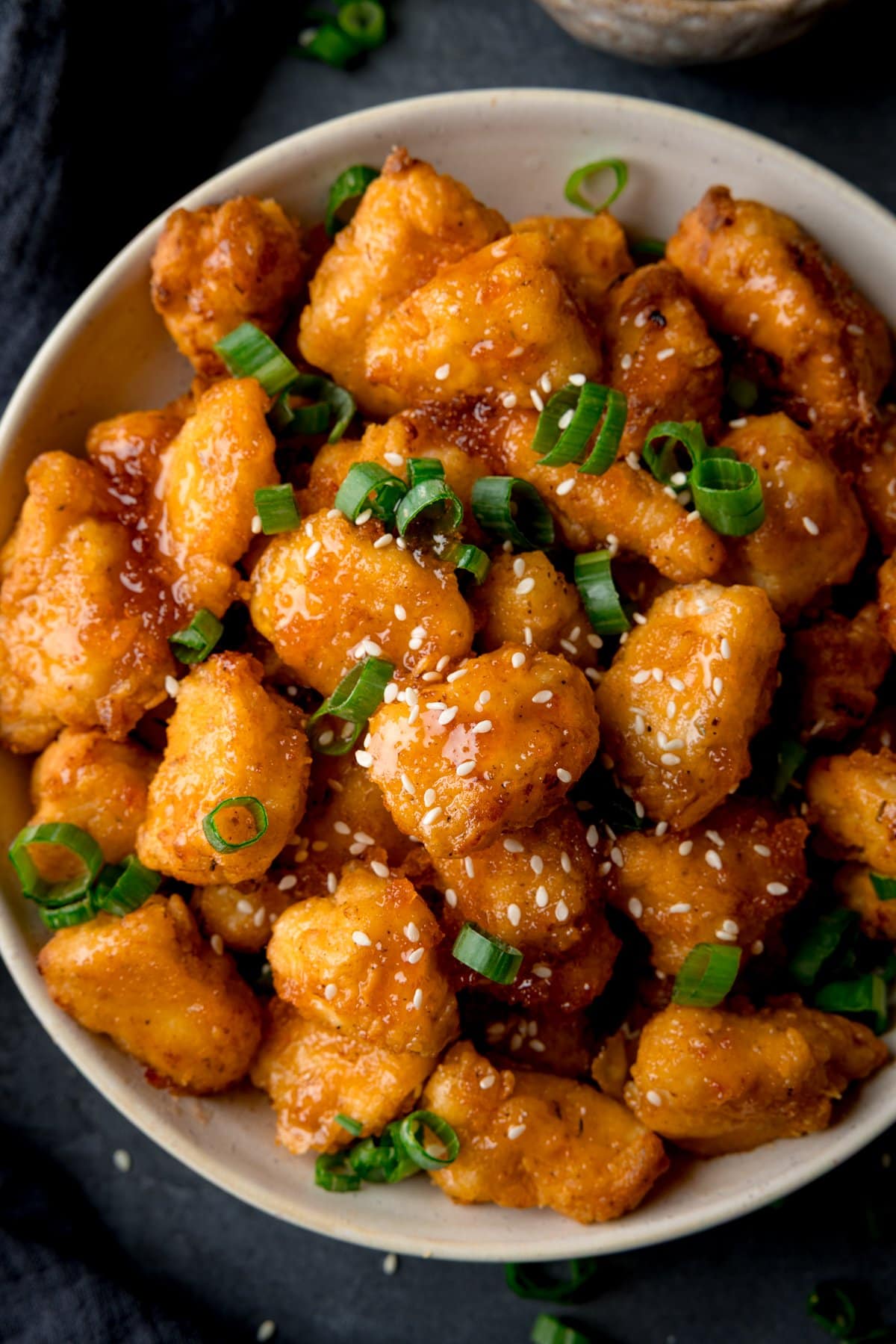 Close-up overhead image of a bowl of crispy Air Fryer hot honey chicken bites garnished with chopped spring onions and sesame seeds.