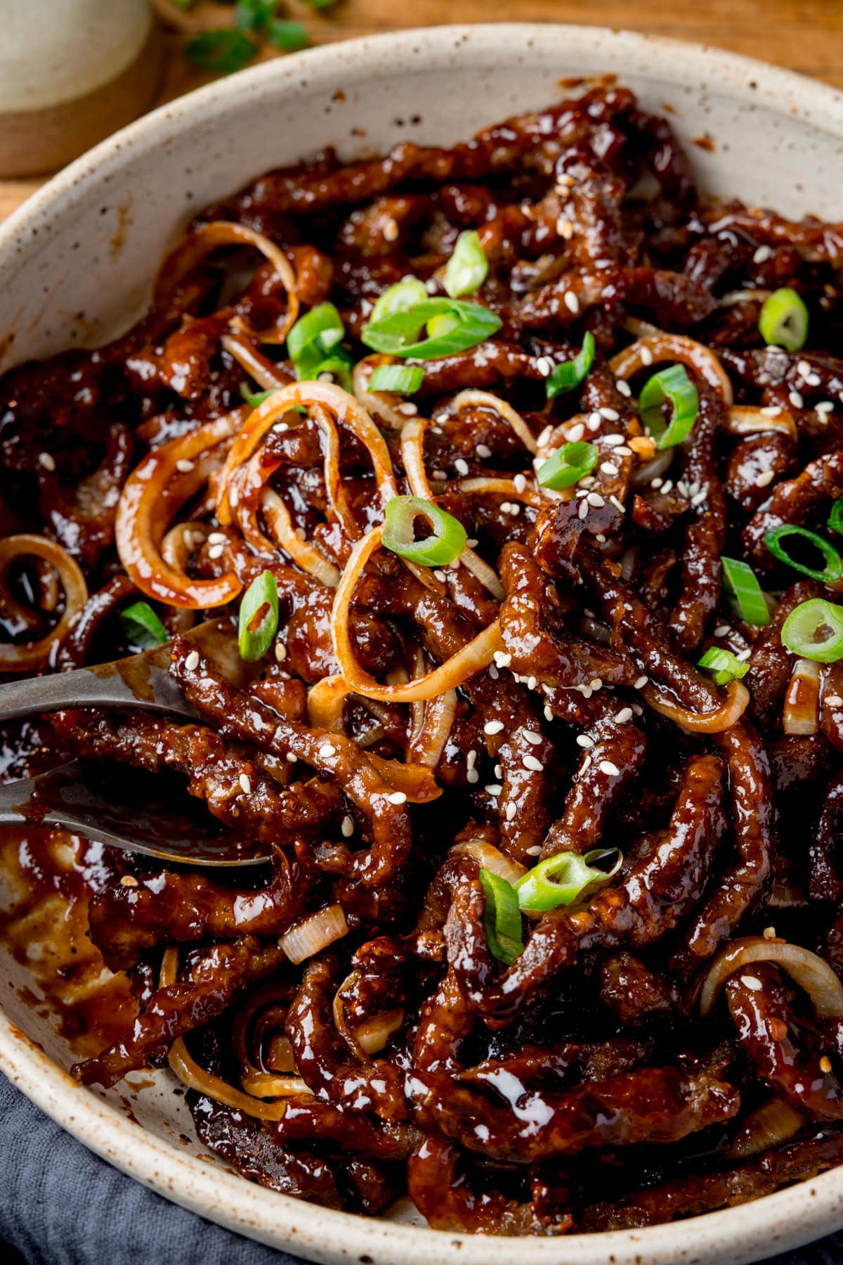 A close up of a light bowl filled with air fryer crispy chilli beef with onions, sesame seeds, and sliced spring onions.