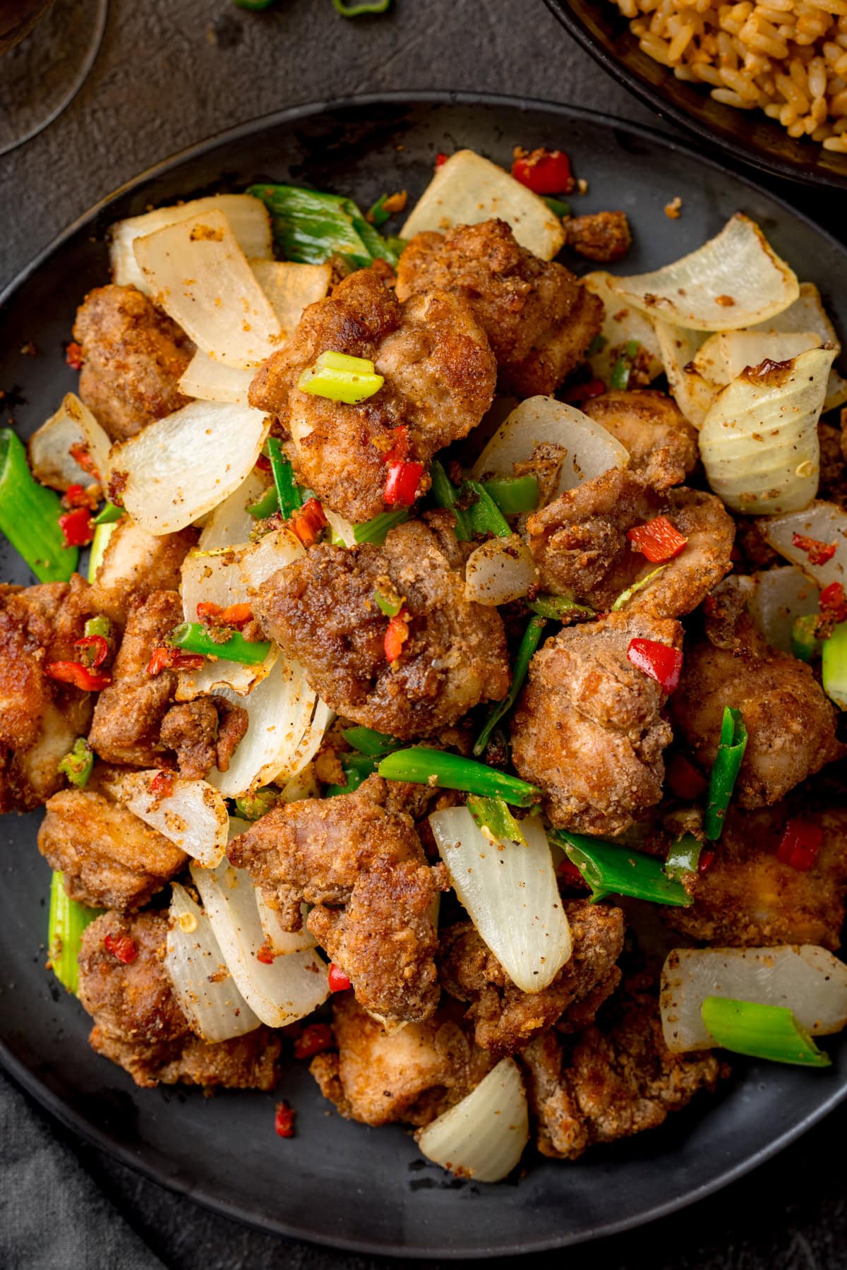 Overhead close up image of a dark plate filled with Air Fryer Chicken with onions, spring onions, and red chillies.