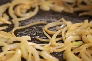 Sliced onions cooking and softening in butter in a dark frying pan.