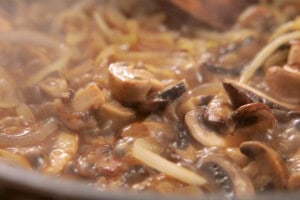 Close-up of sliced mushrooms and onions cooking in a marsala wine in a frying pan.