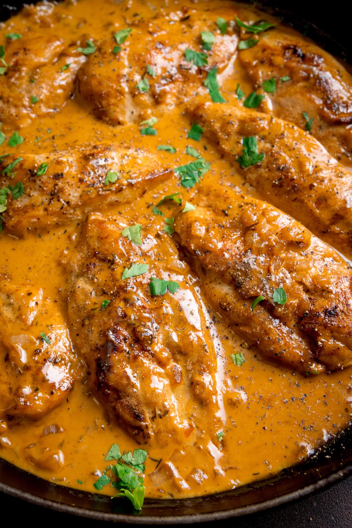 Chicken breasts cooked in a creamy honey mustard sauce, garnished with chopped parsley and black pepper, served in a frying pan.