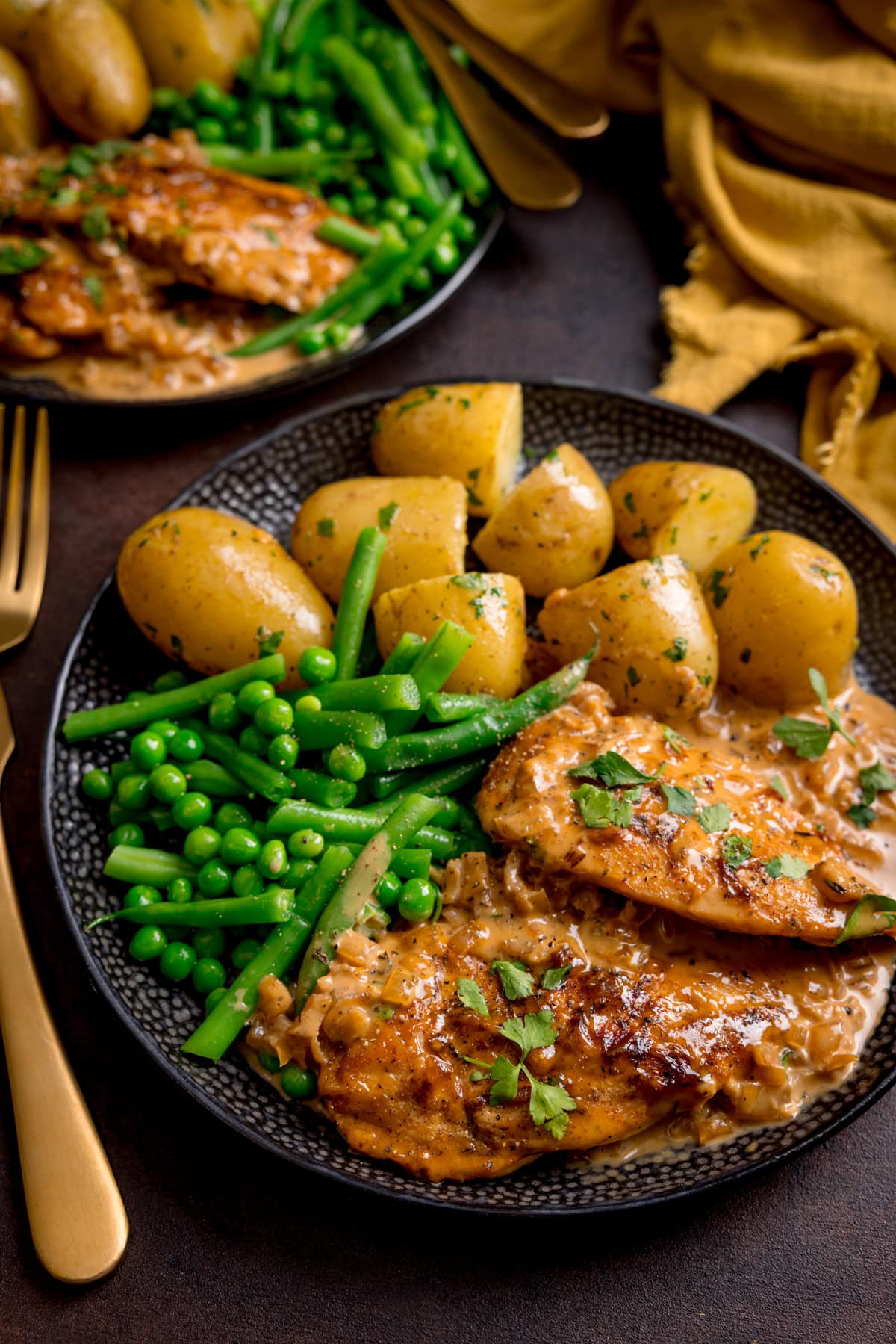 A plate with chicken in creamy honey mustard sauce, boiled potatoes, green beans, and peas, garnished with parsley.