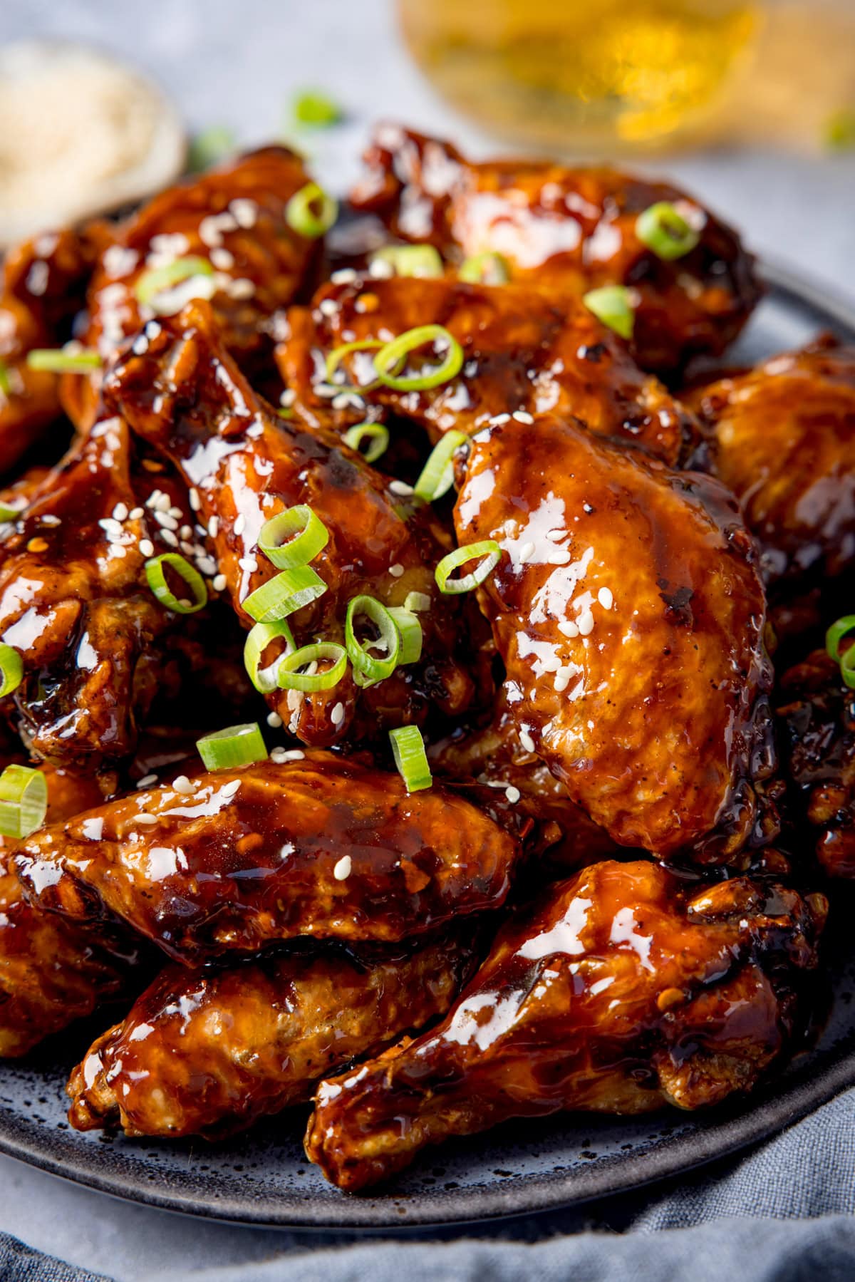 A plate of tamarind chicken wings glazed to perfection, garnished with sliced spring onions and sesame seeds all on a grey plate.