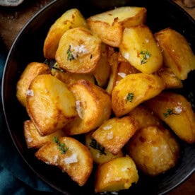 A bowl of golden air fryer roast potatoes, garnished with coarse salt and fresh herbs.