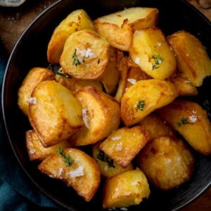 A bowl of golden air fryer roast potatoes, garnished with coarse salt and fresh herbs.