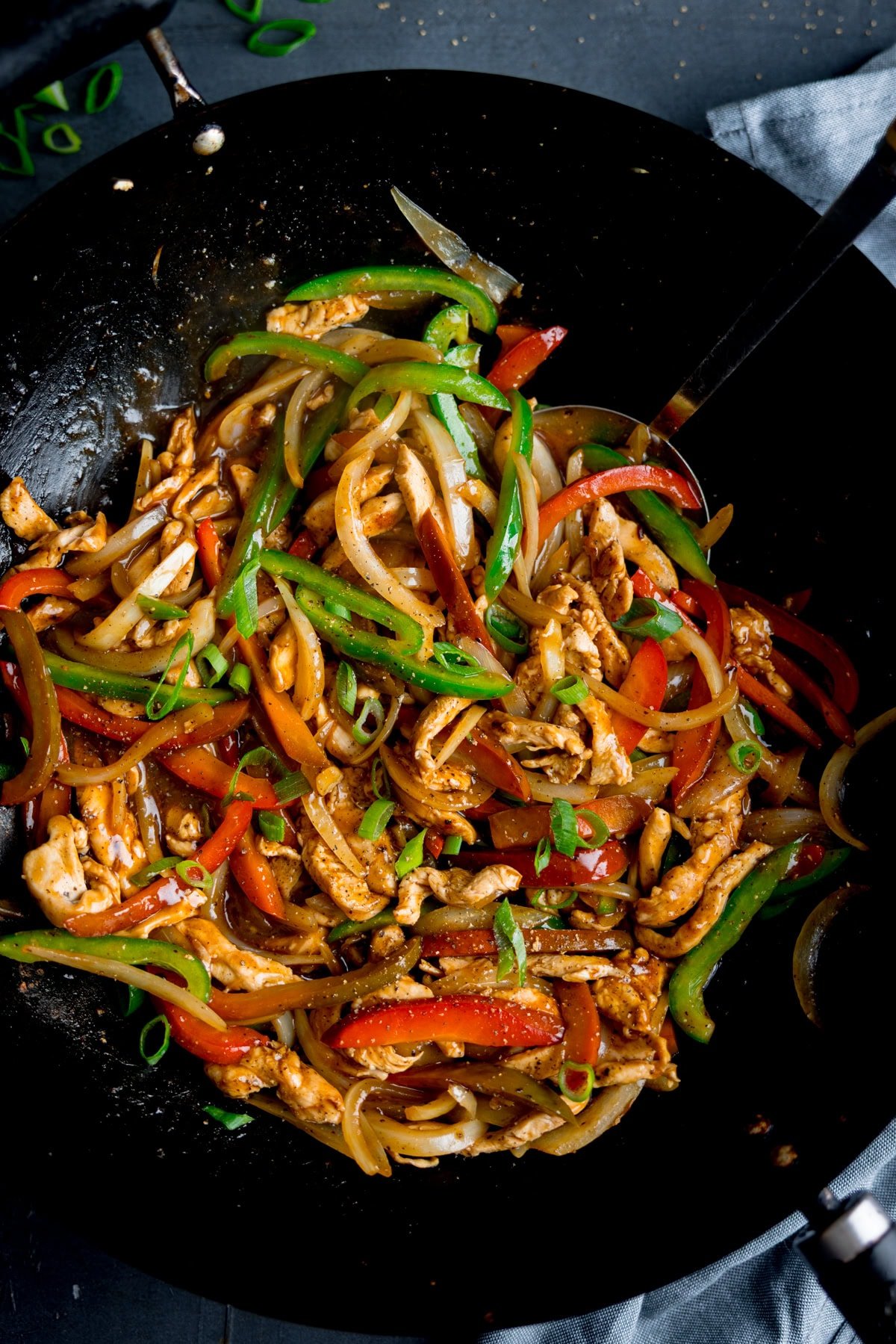 A wok filled with Black Pepper Chicken—stir-fried chicken strips, onions, and red and green peppers, garnished with chopped spring onions.