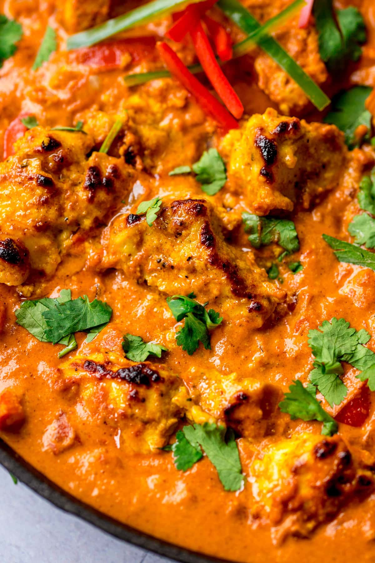 Close-up of chicken tikka masala with chargrilled chicken pieces in creamy masala curry sauce, garnished with fresh coriander and sliced chillies.