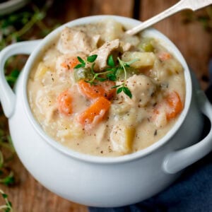 A white bowl filled with creamy chicken pot pie soup containing pieces of chicken, carrots, celery and potatoes, topped with fresh thyme.