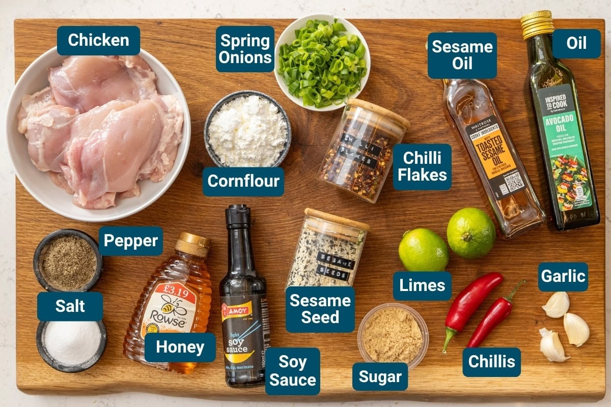 A wooden board displays labelled ingredients for chilli lime chicken, including chicken, spring onions, soy sauce, spices, oil, honey, limes, garlic, and fresh chillies, arranged neatly.