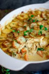 Close up image of a casserole dish with sliced baked potatoes on a creamy chicken and vegetable filling. A spoonful of the dish has been removed.