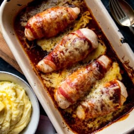 Hunters Chicken - Four bacon-wrapped chicken breasts baked in a rectangular dish with melted cheese and sauce, next to a bowl of mashed potato.