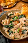 Bowl of creamy chicken rigatoni alfredo pasta with kale, garnished with parsley and served with a slice of garlic bread.