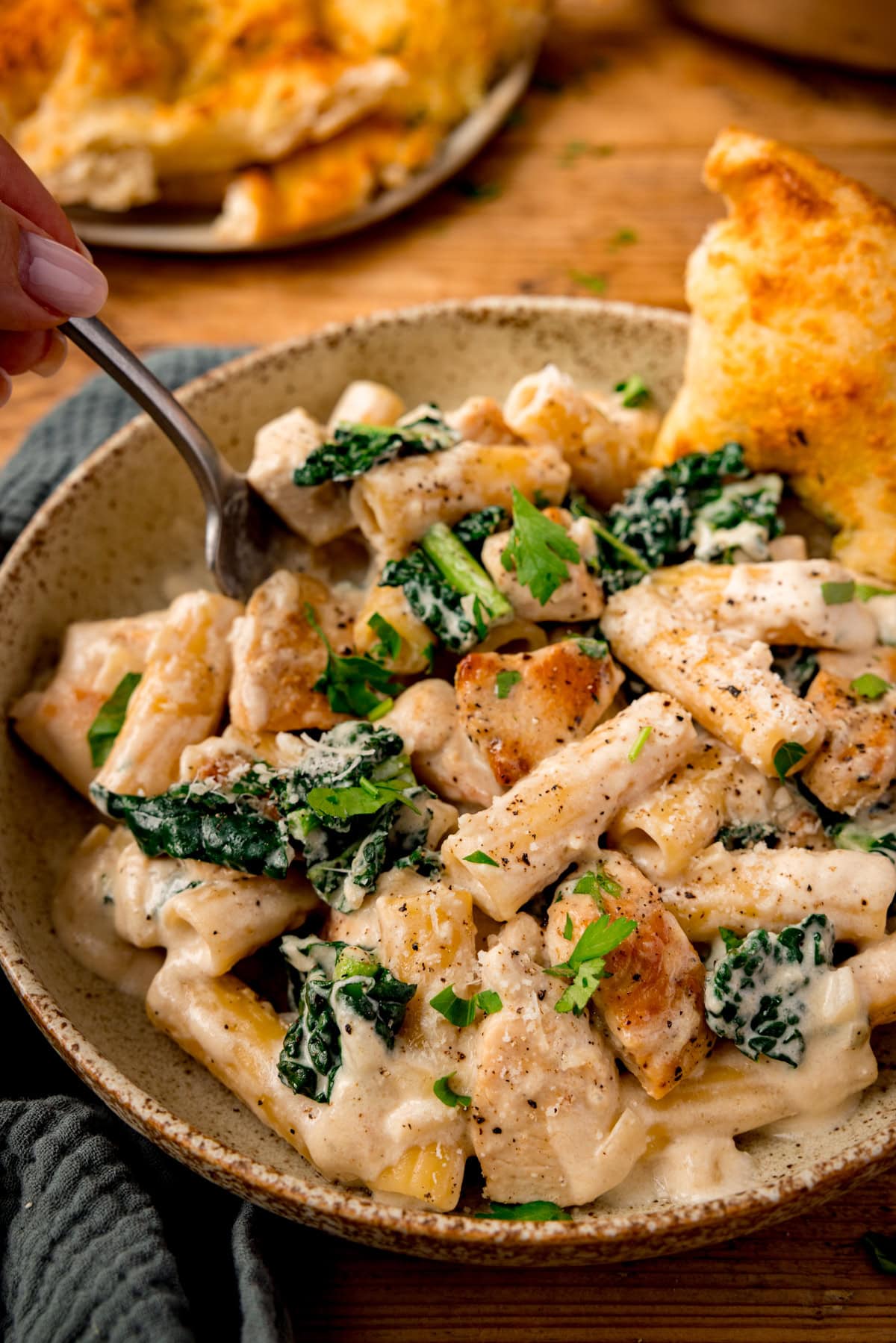 Bowl of creamy chicken rigatoni alfredo pasta with kale, garnished with parsley and served with a slice of garlic bread.