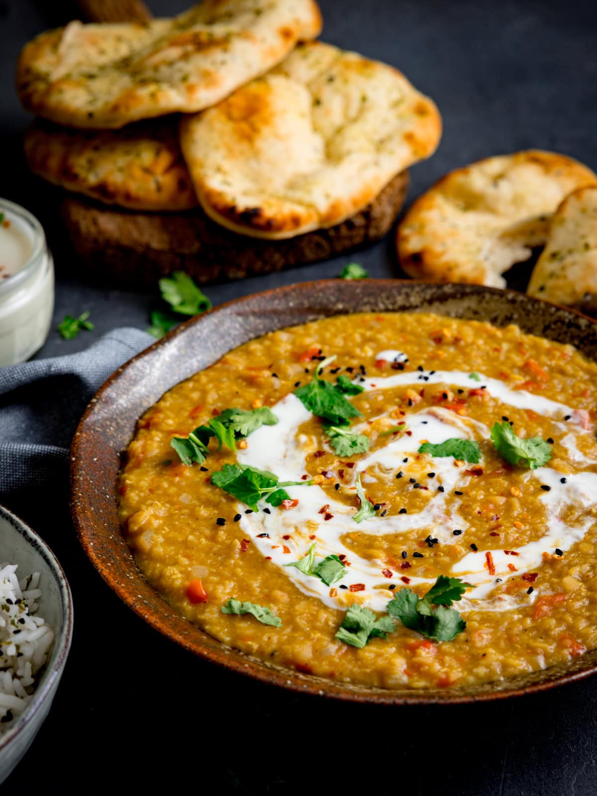 A bowl of red lentil dhal dal garnished with cream and coriander, served with naan bread and a side of rice.