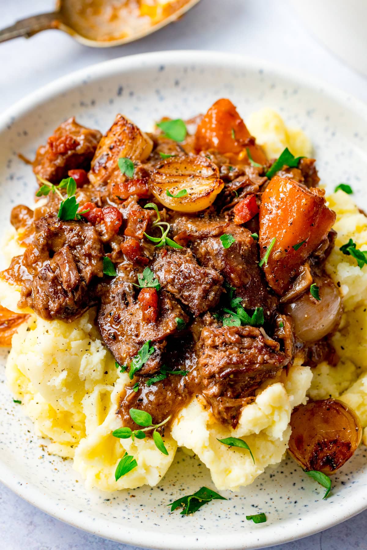 A plate of mashed potatoes topped with beef bourguignon, carrots, onions, and garnished with fresh herbs.