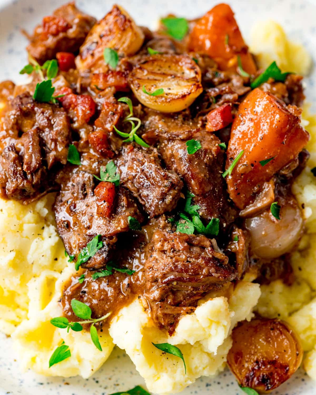A plate of mashed potato topped with beef stew, carrots, onions, and garnished with fresh herbs.