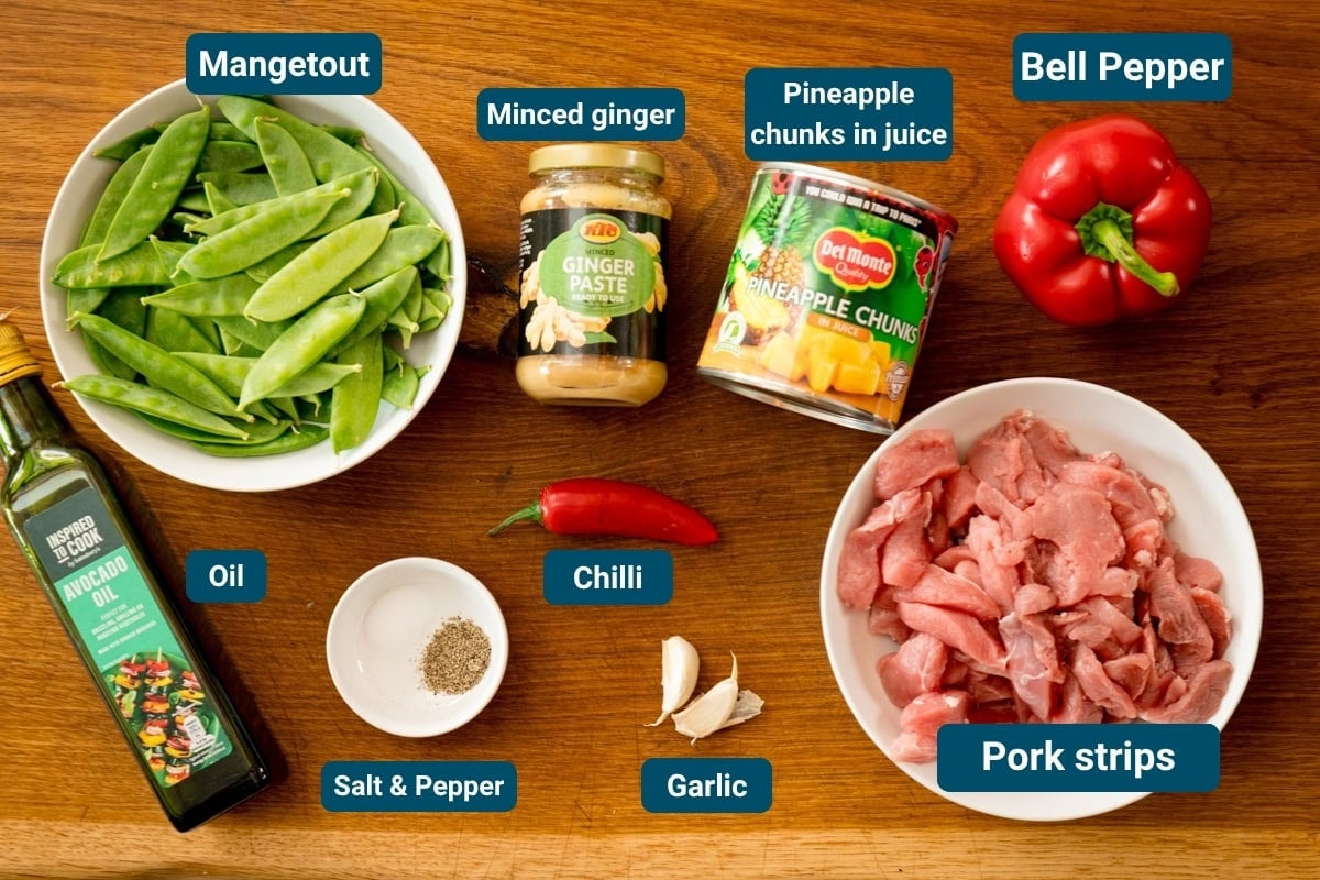 A wooden surface with labeled ingredients: mangetout, minced ginger, pineapple chunks, pepper, oil, salt and pepper, chilli, garlic, and pork strips.